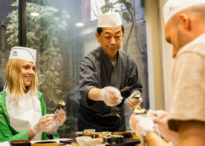 An expert sushi chef guides two guests at a sushi-making class in Tokyo.